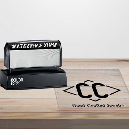 picture of a Multi Surface stamp on wood table next to a clear plastic bag with a black ink impression