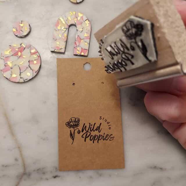 picture of a hand holding wood handle stamp over a brown card label with a black impression for 